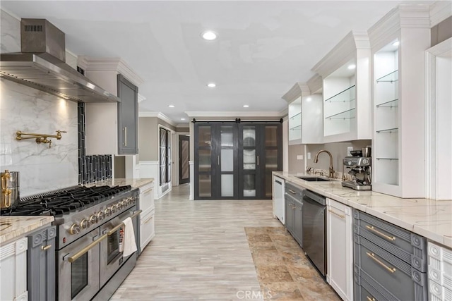 kitchen featuring wall chimney exhaust hood, a sink, appliances with stainless steel finishes, crown molding, and light stone counters