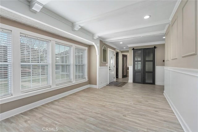 interior space with ornamental molding, a barn door, beamed ceiling, and light wood-style flooring