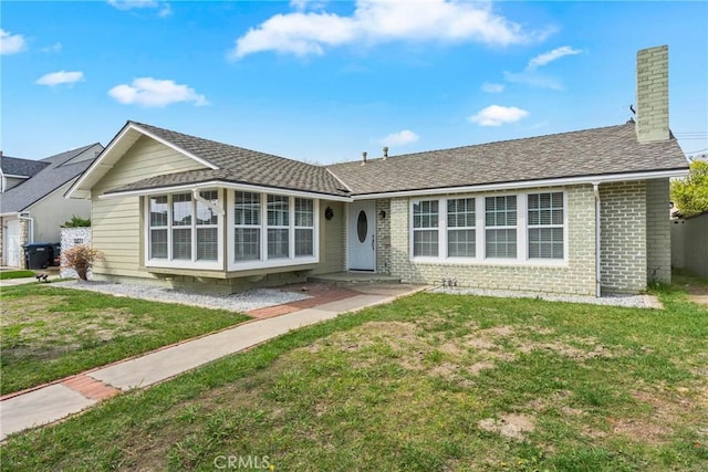 ranch-style house with roof with shingles, a chimney, a front lawn, and brick siding