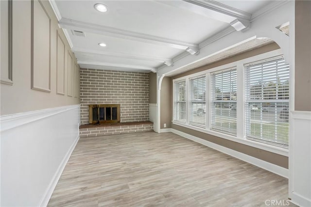 unfurnished living room with light wood finished floors, ornamental molding, beamed ceiling, and a brick fireplace