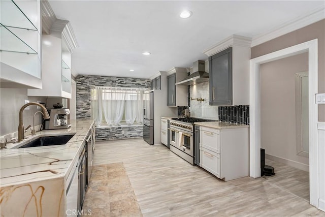kitchen with tasteful backsplash, wall chimney exhaust hood, a sink, light stone countertops, and stainless steel appliances