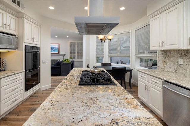 kitchen featuring white cabinets, hanging light fixtures, island exhaust hood, light stone counters, and black appliances