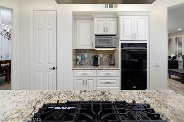 kitchen with double oven, gas stovetop, light stone countertops, white cabinets, and decorative backsplash