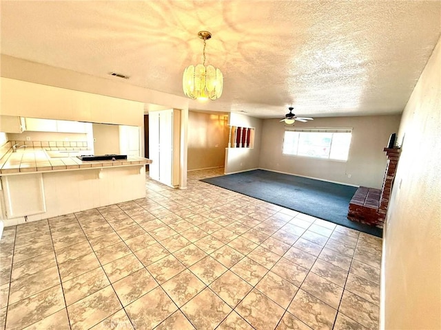 unfurnished living room with ceiling fan with notable chandelier, a textured ceiling, and light tile patterned floors