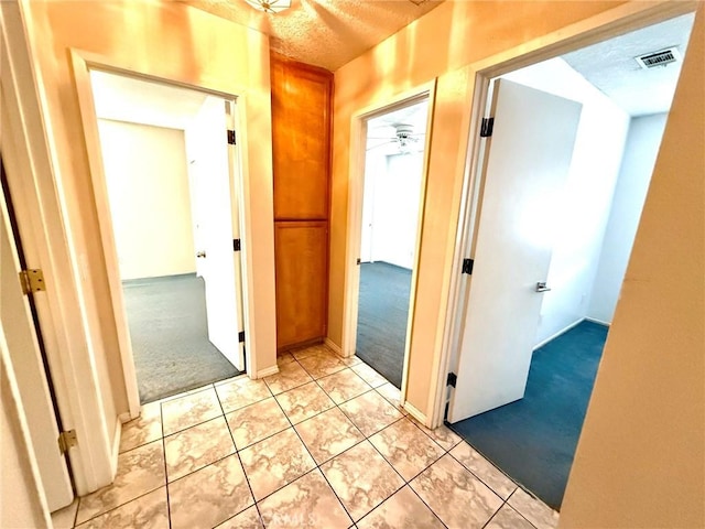 hallway featuring light carpet, visible vents, and a textured ceiling