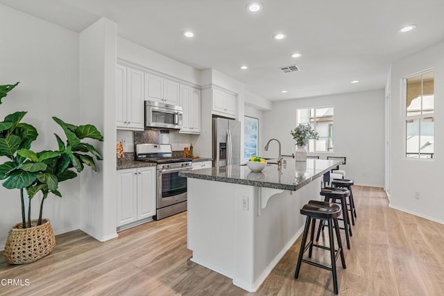 kitchen featuring white cabinetry, stainless steel appliances, a kitchen breakfast bar, a center island with sink, and light wood-type flooring