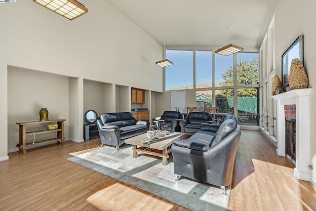 living room with expansive windows, a towering ceiling, light hardwood / wood-style floors, and a brick fireplace