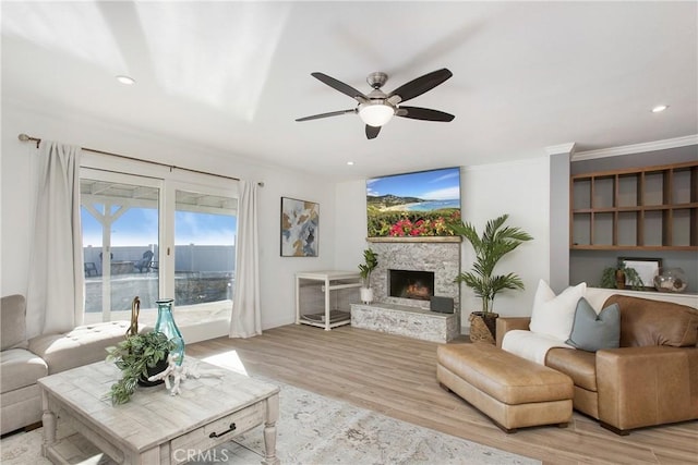 living room featuring a stone fireplace, ornamental molding, ceiling fan, and light wood-type flooring