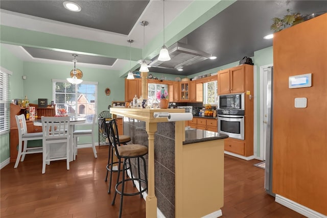 kitchen with dark wood-type flooring, a kitchen breakfast bar, black microwave, decorative light fixtures, and stainless steel oven