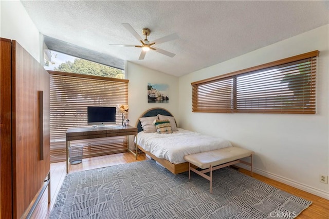 bedroom with vaulted ceiling, hardwood / wood-style floors, ceiling fan, and a textured ceiling