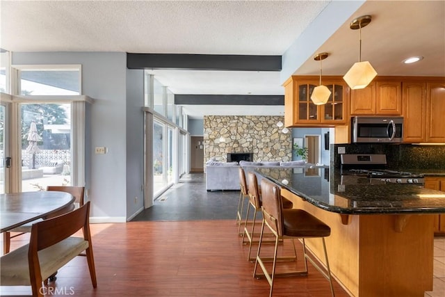 kitchen featuring a textured ceiling, appliances with stainless steel finishes, dark hardwood / wood-style flooring, pendant lighting, and dark stone counters