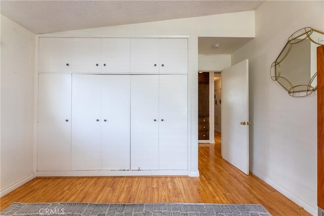 unfurnished bedroom featuring lofted ceiling, light wood-type flooring, and a closet