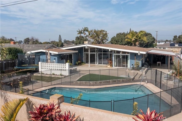 rear view of property featuring a fenced in pool, a patio, and a trampoline