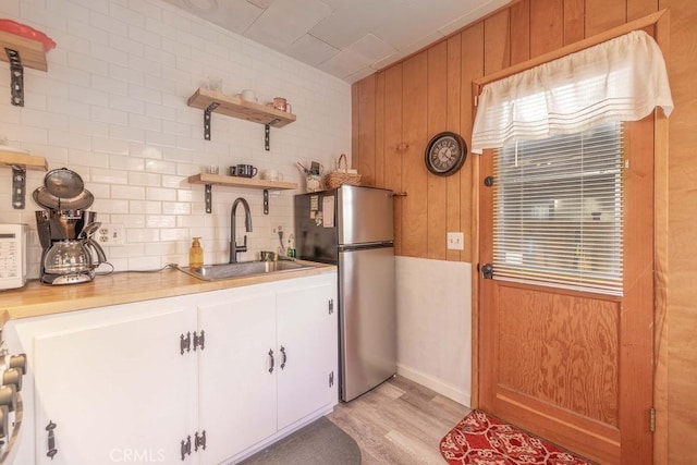 kitchen featuring sink, stainless steel fridge, white cabinetry, backsplash, and light hardwood / wood-style floors