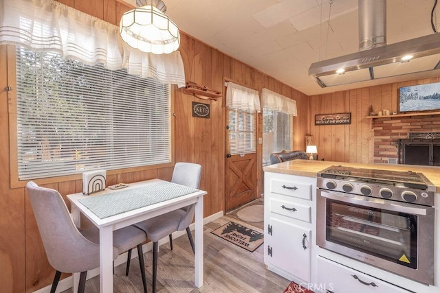 kitchen with stainless steel range oven, butcher block counters, wooden walls, range hood, and white cabinets