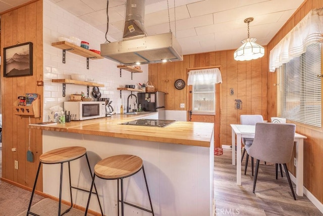 kitchen featuring butcher block countertops, a breakfast bar area, island range hood, black electric cooktop, and kitchen peninsula