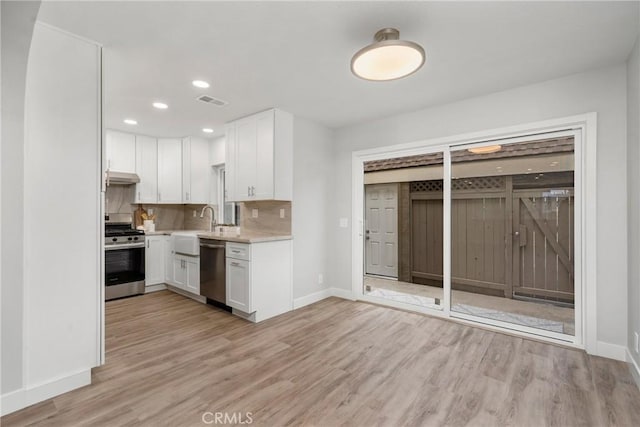 kitchen featuring white cabinetry, appliances with stainless steel finishes, decorative backsplash, and light wood-type flooring