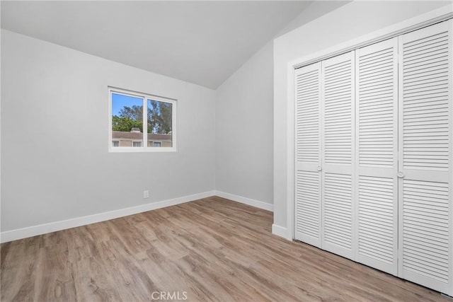 unfurnished bedroom with light hardwood / wood-style floors, vaulted ceiling, and a closet