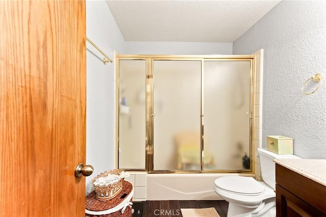 full bathroom with shower / bath combination with glass door, hardwood / wood-style flooring, vanity, toilet, and a textured ceiling