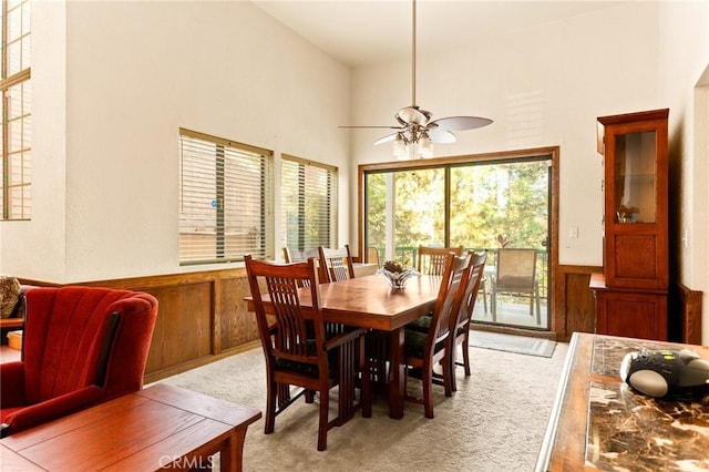 carpeted dining area featuring ceiling fan, a towering ceiling, and wooden walls