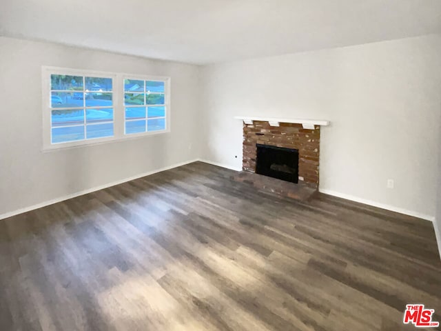 unfurnished living room with a brick fireplace and dark hardwood / wood-style flooring