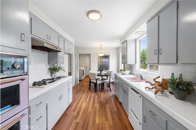 kitchen featuring gray cabinetry, tile countertops, separate washer and dryer, hanging light fixtures, and white appliances