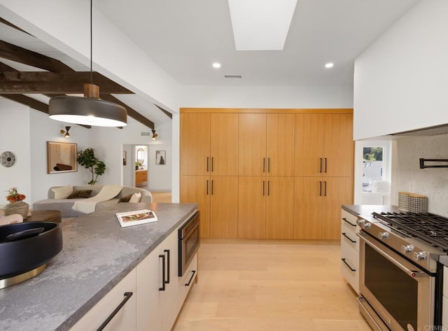 kitchen with appliances with stainless steel finishes, pendant lighting, a skylight, beam ceiling, and light hardwood / wood-style flooring