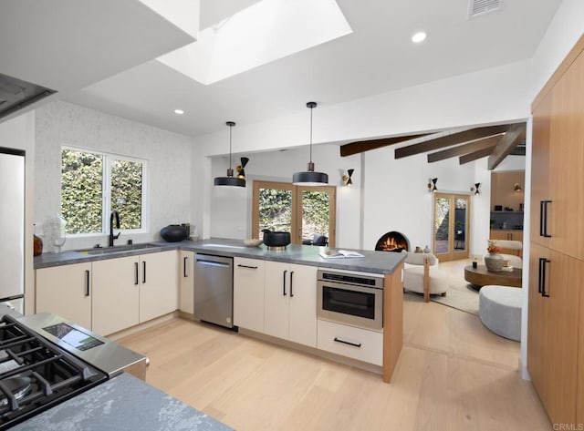 kitchen with a skylight, decorative light fixtures, sink, kitchen peninsula, and stainless steel appliances