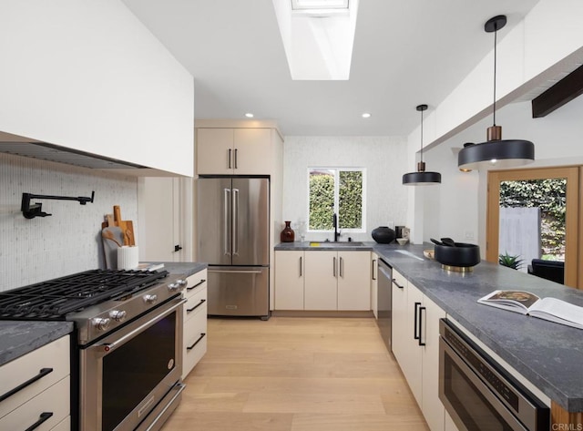 kitchen featuring pendant lighting, a skylight, sink, dark stone countertops, and stainless steel appliances