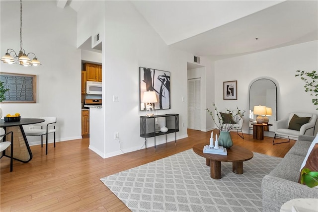 living room featuring an inviting chandelier, high vaulted ceiling, and light wood-type flooring