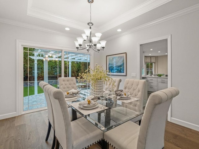 dining room featuring an inviting chandelier, a tray ceiling, wood-type flooring, and ornamental molding