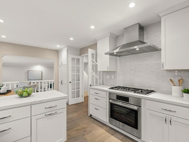 kitchen featuring wall chimney range hood, appliances with stainless steel finishes, tasteful backsplash, light hardwood / wood-style floors, and white cabinets