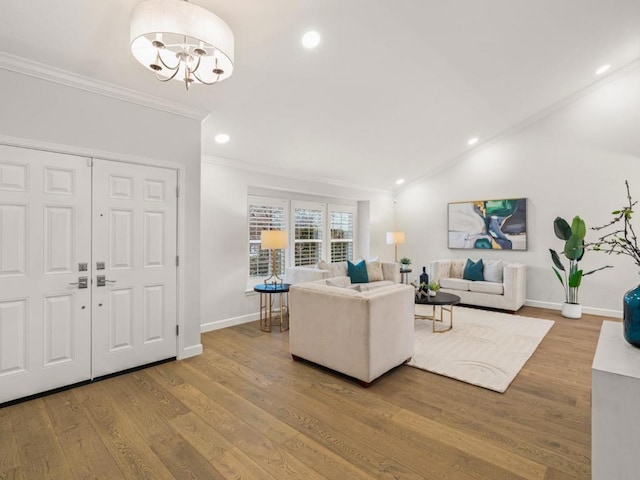 living room with an inviting chandelier, ornamental molding, wood-type flooring, and vaulted ceiling