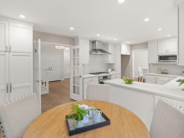 kitchen featuring white cabinetry, wall chimney range hood, decorative backsplash, and appliances with stainless steel finishes