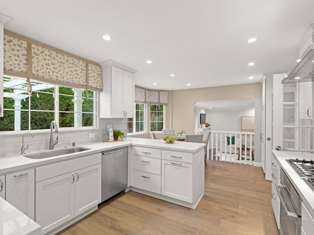 kitchen featuring sink, light hardwood / wood-style flooring, stainless steel dishwasher, kitchen peninsula, and white cabinets