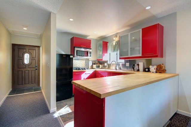 kitchen featuring black appliances, sink, wooden counters, light colored carpet, and kitchen peninsula