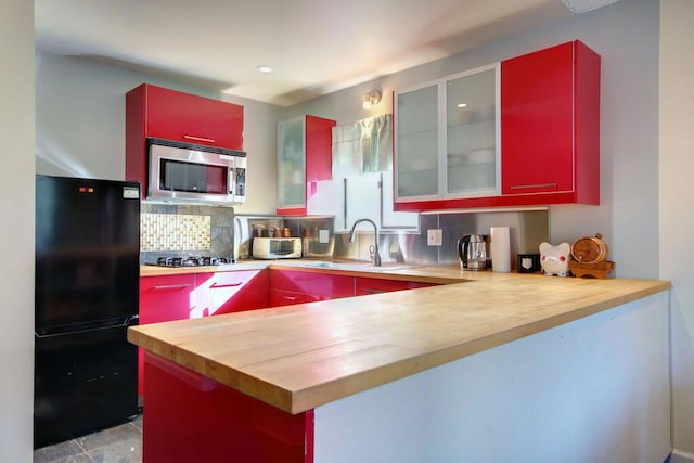 kitchen with sink, wooden counters, decorative backsplash, kitchen peninsula, and stainless steel appliances