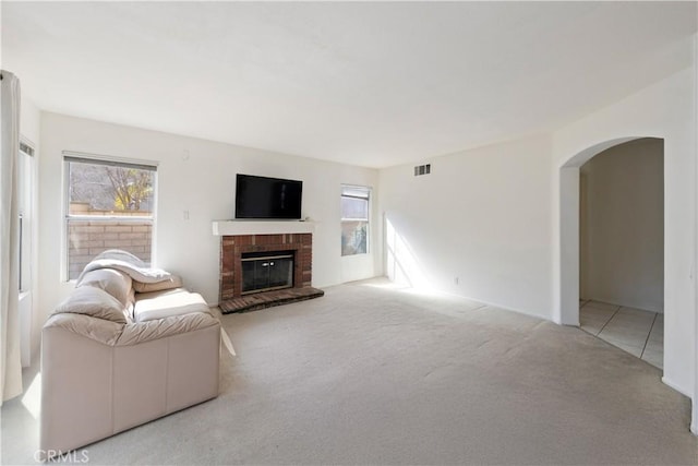 living area featuring a healthy amount of sunlight, a brick fireplace, arched walkways, and light colored carpet