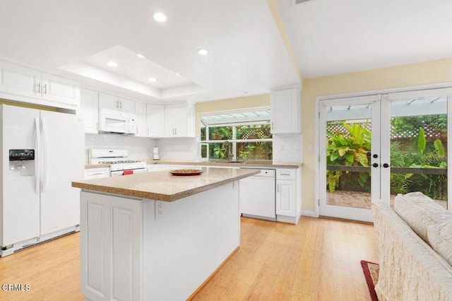 kitchen with white appliances, a center island, white cabinets, a raised ceiling, and light wood-type flooring