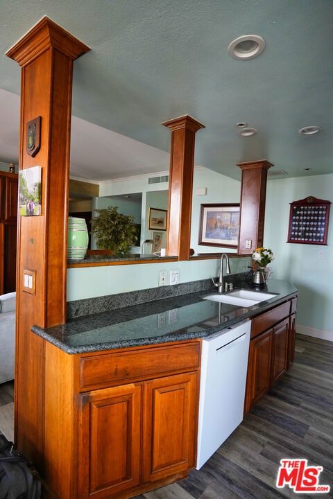 kitchen with decorative columns, dishwasher, sink, dark hardwood / wood-style flooring, and dark stone counters