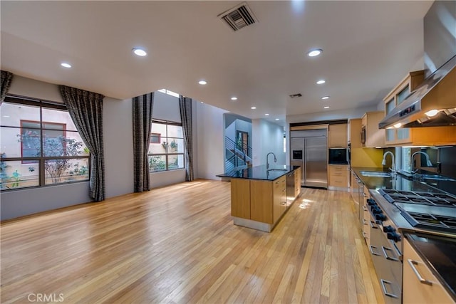 kitchen with high end appliances, sink, a kitchen island with sink, and light wood-type flooring