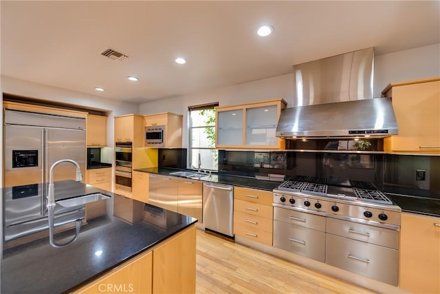 kitchen featuring sink, built in appliances, light wood-type flooring, light brown cabinets, and wall chimney range hood