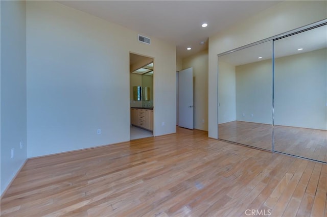 unfurnished bedroom with a closet, connected bathroom, and light hardwood / wood-style flooring