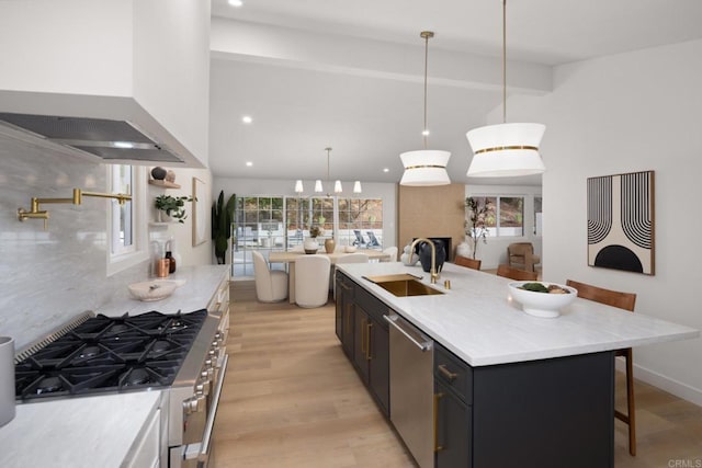 kitchen with sink, custom exhaust hood, appliances with stainless steel finishes, pendant lighting, and a kitchen island with sink