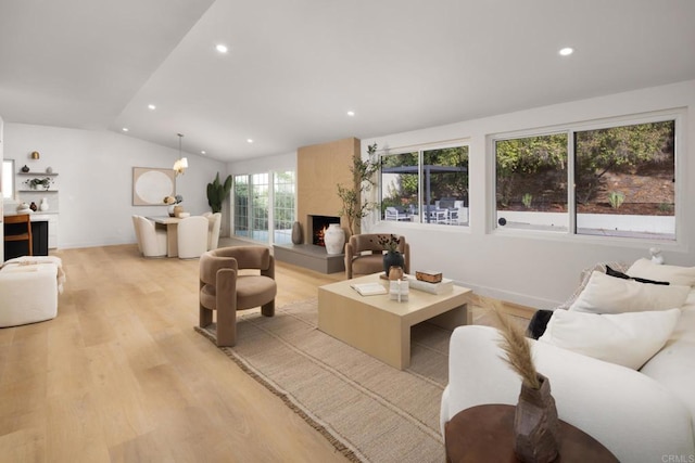 living room with vaulted ceiling, a fireplace, and light hardwood / wood-style floors