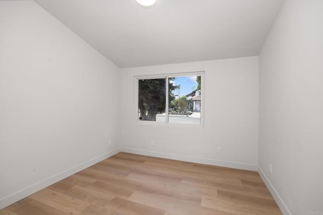 spare room featuring lofted ceiling and light hardwood / wood-style flooring