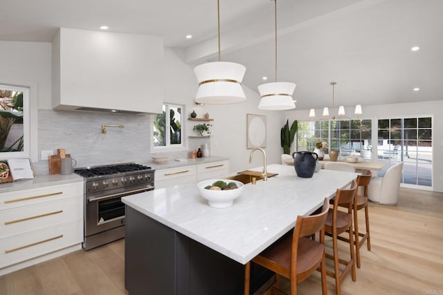 kitchen featuring premium range hood, stainless steel range, a kitchen island with sink, and white cabinets