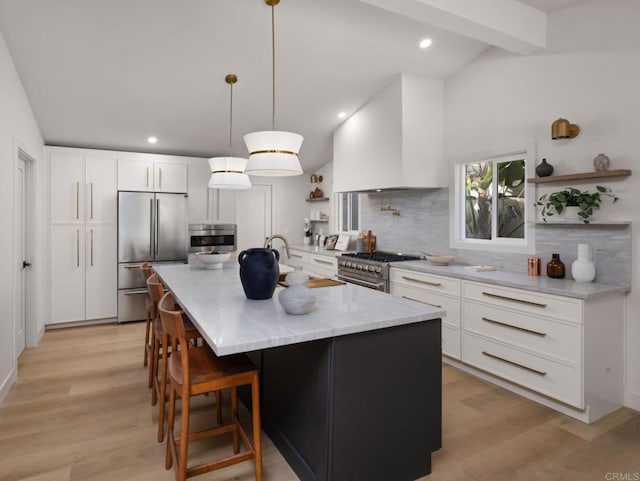 kitchen featuring premium range hood, an island with sink, white cabinets, hanging light fixtures, and high end appliances