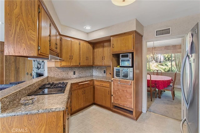 kitchen with tasteful backsplash, a notable chandelier, light stone counters, and appliances with stainless steel finishes