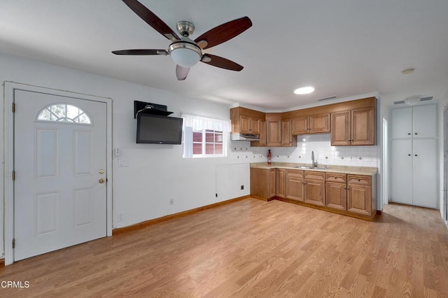 kitchen with tasteful backsplash, brown cabinetry, light countertops, light wood-style floors, and a sink